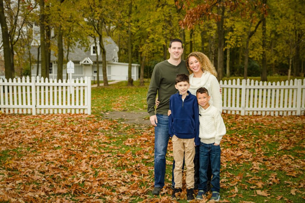 There is a family session at the lighthouse, with beautiful fall colors along a white fence. 